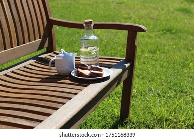 Coffee Pitcher, Glass Bottle Of Homemade Lemonade And Cake On Wooden Bench, Blurred Green Grass Background. Outdoor Coffee Break. Picnic, Garden Party Snack, Relaxation Concept. No People.