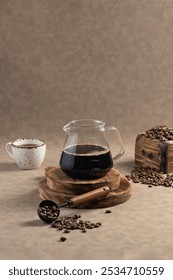 Cafetera con café negro y frijoles: una olla de vidrio llena de café negro recién hecho, colocada en una tabla de madera. Acompañado de una taza de cerámica y una cucharada de granos de café.
