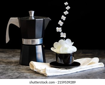 Coffee pot and coffee cup with fresh flowers as foam and flying as steam on black background. Creative floral spring bloom bw concept. Black and white still life natural visual trend