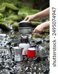 Coffee pot and metal cup on big stone against backdrop of mountain river. Coffee pot on stone plate over blurred nature background.