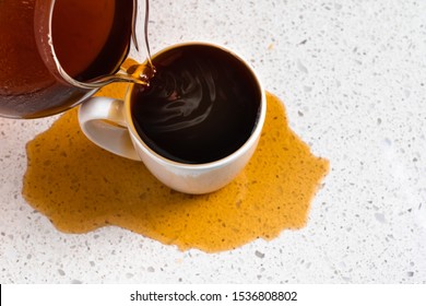 Coffee pours into mug overflows and spills over with too much spilling on white kitchen counter