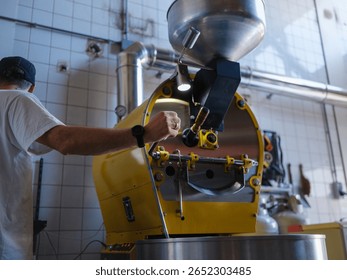 Coffee roaster operator using professional yellow roasting machine with stainless steel components, monitoring roasting process in modern commercial coffee facility