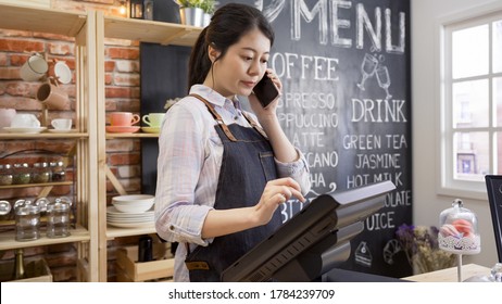 coffee shop assistant taking order on mobile phone in cafe restaurant. young girl waitress in apron standing in counter using point of sale terminal in store while listening to customer talking - Powered by Shutterstock