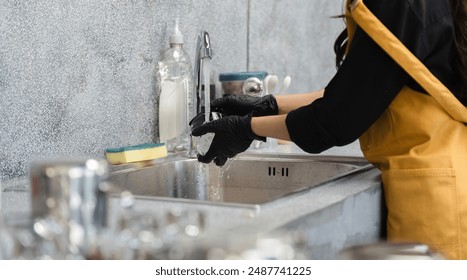 Coffee Shop Cleaning Staff Washing Dishes at Sink with Gloves and Apron in Modern Cafe Kitchen - Powered by Shutterstock