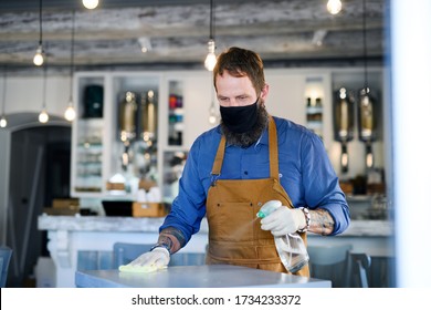 Coffee Shop Man Owner Working With Face Mask And Gloves, Disinfecting Tables.