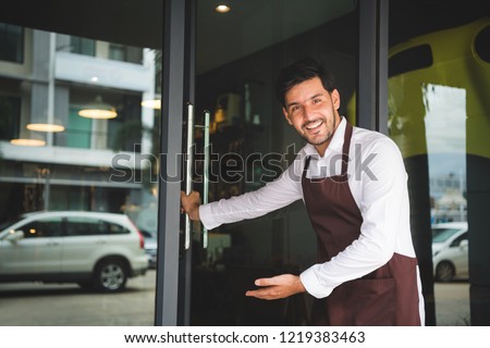 The coffee shop owner is opening the door, inviting customers to his shop. Setup studio shooting.