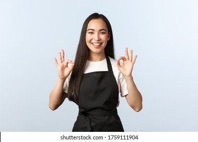 Coffee Shop, Small Business And Startup Concept. Smiling Attractive Korean Female Barista, Waitress In Cafe, Black Apron Assure Clients, Show Okay Sign And Grinning, No Problem, Guarantee Quality