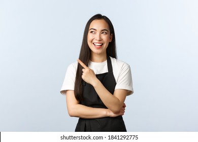 Coffee Shop, Small Business And Startup Concept. Cheerful Smiling Asian Female Barista At Cafe Counter, Wear Black Apron, Pointing And Looking Upper Left Corner Joyful, Showing Promo