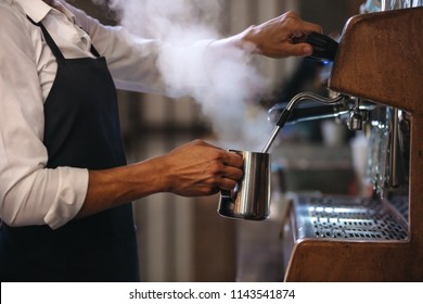 Coffee shop worker preparing coffee on steam espresso coffee machine. Cropped shot of man working in coffee shop wearing an apron. - Powered by Shutterstock