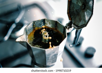 Coffee squirts out of an Italian moka pot with energy. Italian tradition and spitting out espresso. Splashes of black coffee spurting out from the spout and open moka pot stock photo.