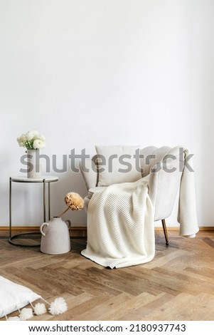 Coffee table with flowers near beige armchair with pillow and plaid. Modern design of living room with home decor and new furniture in apartment
