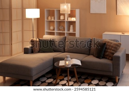 Coffee table with lantern, cozy sofa and glowing lamps in interior of living room