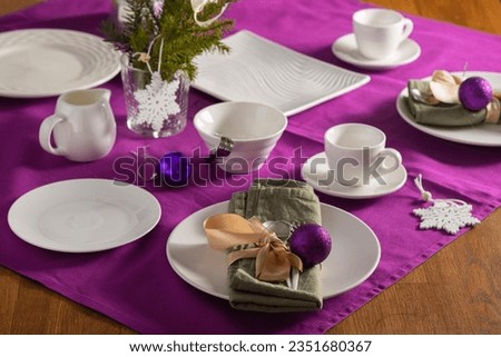 Coffee table setting with white tableware in Christmas style on a table with a purple tablecloth. Merry Christmas concept. Receiving guests, coffee serving