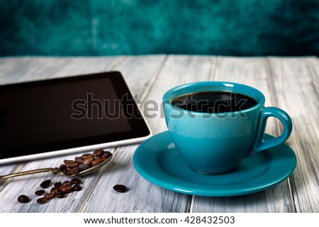 Coffee and tablet on the table. Pause and coffeetime. Blue cup and background.