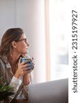 Coffee, thinking and woman in home office with laptop, daydreaming and enjoy peaceful remote work break. Freelance, relax and female person with tea while working online on proposal plan or project