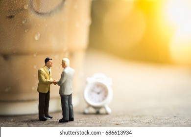 Coffee, Time And Business Cooperation Concept. Two Businessman Miniature Figures Meet And Hand Shake On Wooden Table Close To A Plastic Cup Take Away Of Iced Coffee And Mini Clock Toy.