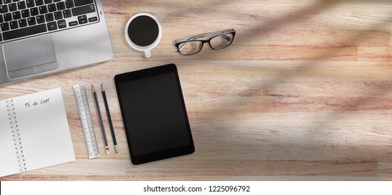 Coffee Time Concept Design For Banner, Top View Of Modern Office Desk Wooden Table Workplace With Laptop, Tablet With Office Supplies, Glasses And Coffee. Morning Sun Cast On Table With Copy Space.