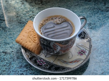 Coffee time elements - a colorful cup of coffee, a biscuit and a jar on a blue surface 