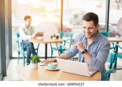 Coffee Time. Handsome Young Man In Cafe With Big Window. Man With Cup Of Coffee. Man Using Laptop And Smiling