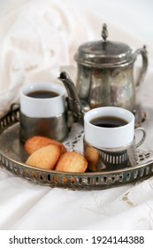 coffee in vintage silver coffee pot and cups with madelens on table with antique tablecloth