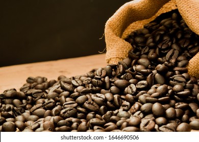 coffee wallpaper, closeup dark brown roasted coffee beans background and coffee sack bag on wooden table for the coffee shop background lifestyle idea with copy space