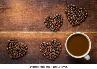 Coffee in white cup with heart design from coffee beans on wooden background.