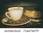 Coffee in a white cup. Spilled coffee beans. Sweet dessert on a plate of coffee. In the dark with side light and analog effect in retro - vintage style

