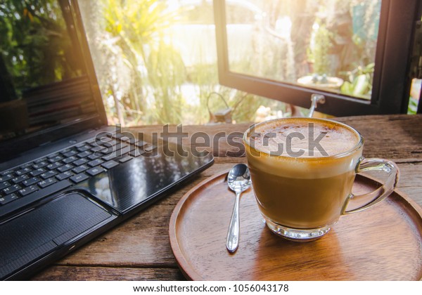 Coffee in the wooden tray by the window and\
notebook computer on the wood table in the cafe. The back is\
blurred and there is light\
through.