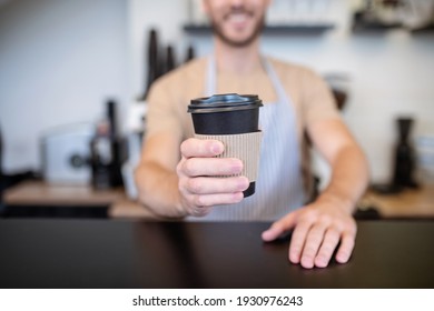 Coffee For You. Paper Cup Of Coffee With Lid In Outstretched Hand Of Barista Standing Behind Bar Counter In Coffee Shop