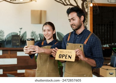 Coffeehouse Couple with 'Open' sign, smiling service, inviting customers into the friendly café atmosphere. Pair of baristas, joyful in service, poised to greet patrons in warm café setting - Powered by Shutterstock