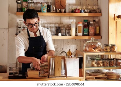 Coffeeshop Barista Cleaning Up Counter And Restocking Supplies