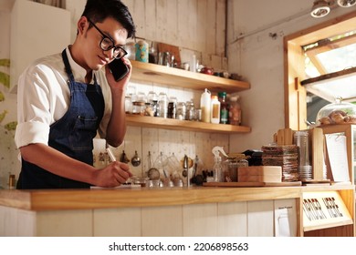 Coffeeshop Waiter Talking On Phone With Customer And Writing Down Order Details