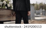 Coffin, hands and man walking at funeral ceremony outdoor with pallbearers at tomb. Death, grief and person carrying casket at cemetery, graveyard or family service of people mourning at windy event