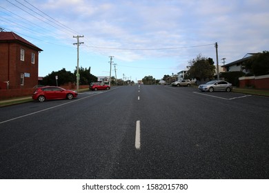 Coffs Harbour, NSW / Australia - July 24th 2019 - A Wide Country Road With Cars Parked Along And Telegraph Poles 