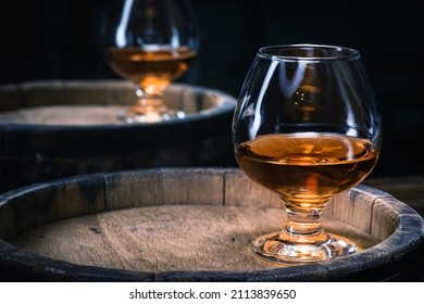 Cognac brandy in glass of amber color stands on old wooden barrel with brandy in wine cellar close-up with copy space. Brandy from old barrel in glass. - Shutterstock ID 2113839650
