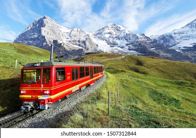Ein Zahnradzug fährt auf der Eisenbahn von Jungfraujoch (oben in Europa) nach Kleine Scheidegg auf dem grünen Grasberg mit Eiger, Monch 