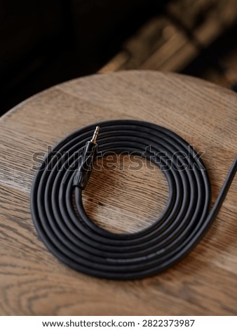 A coiled black professional audio cable with a jack plug rests on an oak stool.