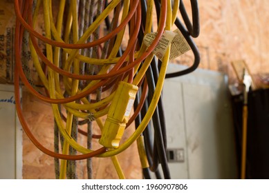 Coiled Mess Of Tangled Extension Power Cords Hanging On Shop Wall