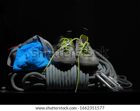 Coiled rope blocked by spiral knot, rock climbing shoes, carabiners, harness belt and blue chalk bag  isolated  on dark background. Main alpinist equipment or climbing tools.
