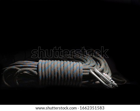 Coiled rope blocked by spiral knot with carabiners isolated  on dark background. Basic alpinist equipment or climbing tools: rope and locking carabiners.