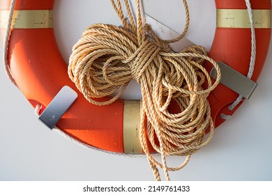 Coiled rope on a boat. Yellow rope and an orange lifebuoy on white wall of a sailboat of marina. Classic yacht or nautical vessel lifeguard resque equipment. 