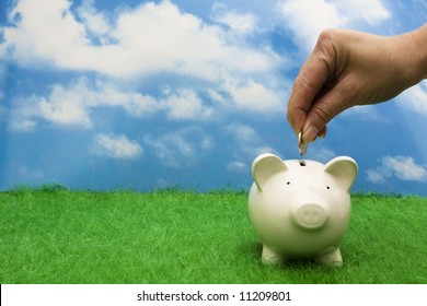 Coin bank sitting on grass with hand putting in a coin - Shutterstock ID 11209801