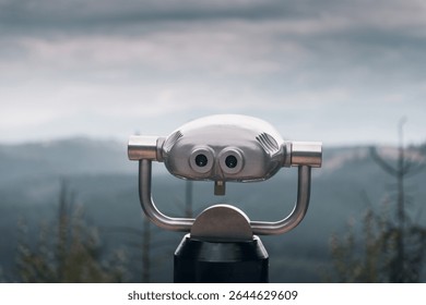 Coin operated binoculars on top of the mountain. Metal binoculars overlooking Carpathian mountains landscape. Selective focus: shiny metal tower viewer and unfocused mountains in the background.