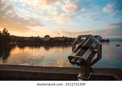 Coin operated binoculars or telescope for tourists. Summer sunrise, dramatic sky, lake water and buildings in the background, shallow depth of field, no people. - Powered by Shutterstock