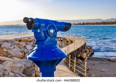 Coin operated telescope overlooking beach and seafront of maritime city with wooden bridge, sea, buildings and silhouette of mountains in the background. Horizontal shot. - Powered by Shutterstock