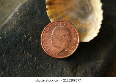Coin and shell on a dark stone. Swedish coin. 2 Kronor Carl XVI Gustaf obverse. Sweden 13.02.2022.      .