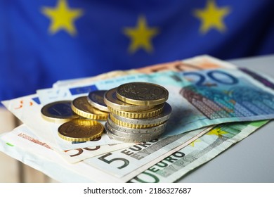 Coins and banknotes on table against European Union flag, closeup