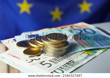 Coins and banknotes on table against European Union flag, closeup
