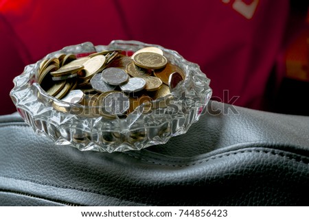 coins in a beautiful ashtray on dark red background
