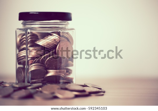 A\
lot coins in glass money jar against white\
background.